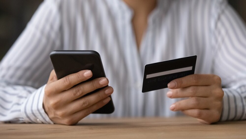 Close up woman paying online by credit card, using smartphone, sitting at wooden desk, young female holding phone, browsing banking service, checking balance, shopping, making internet payment