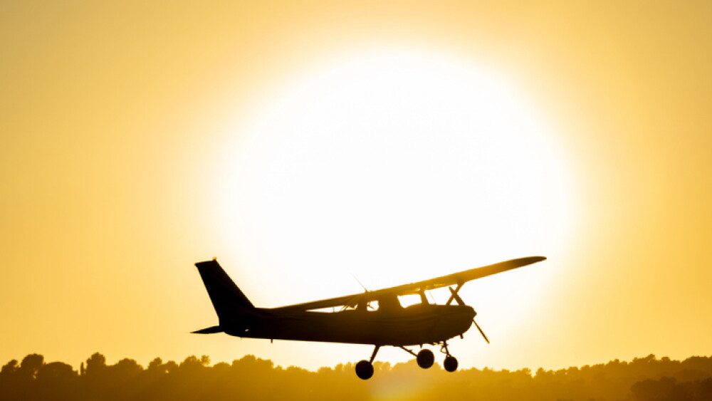 Silhouette of a small propeller plane landing or taking off on the runway backlit under a yellow sun at sunset at Sabadell airport.