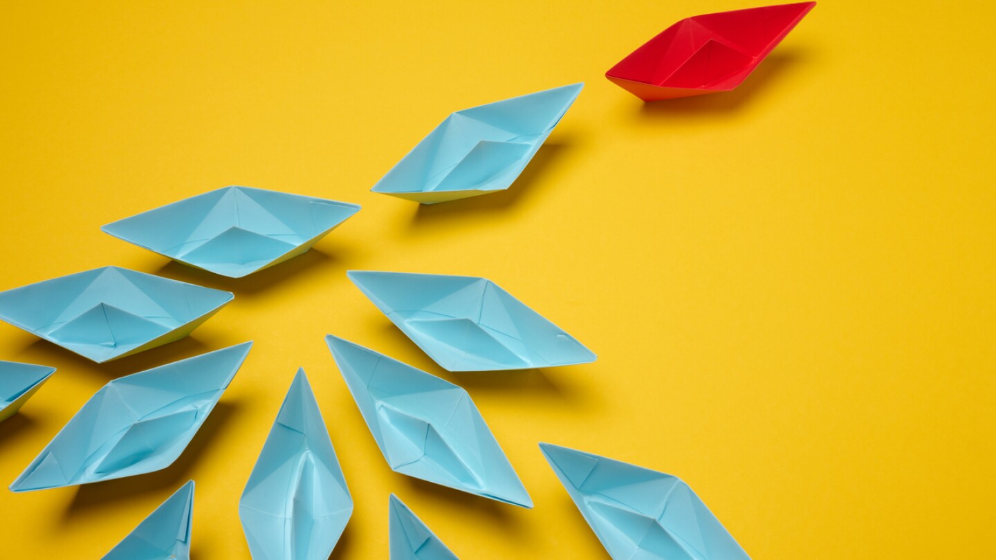 Group of blue paper boats following on red on yellow background, mass manipulation