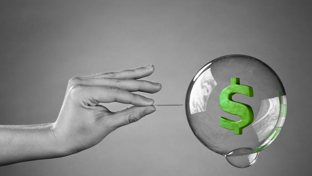 A hand about to burst a money bubble with a pin. Metaphor for an economic or financial bubble crisis.