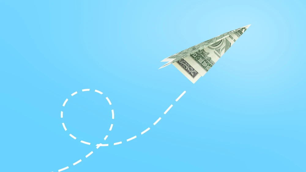 Dollar paper airplane flying against blue background, business concept