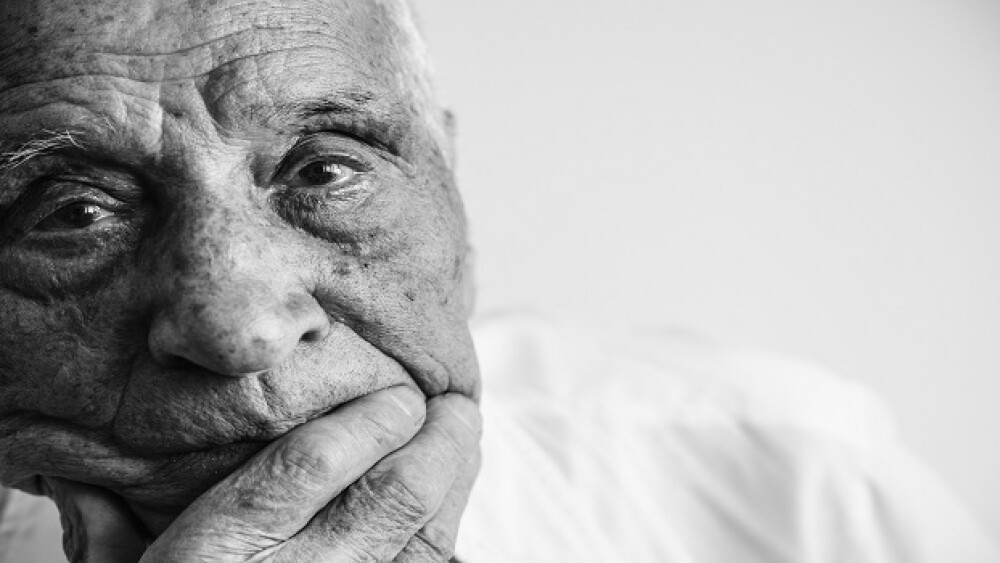 An old man looking at camera, covering his mouth with his hand. Black and white photo.