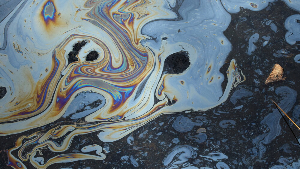 Iridescent colors abstract shapes on tar water surface of natural asphalt pit.