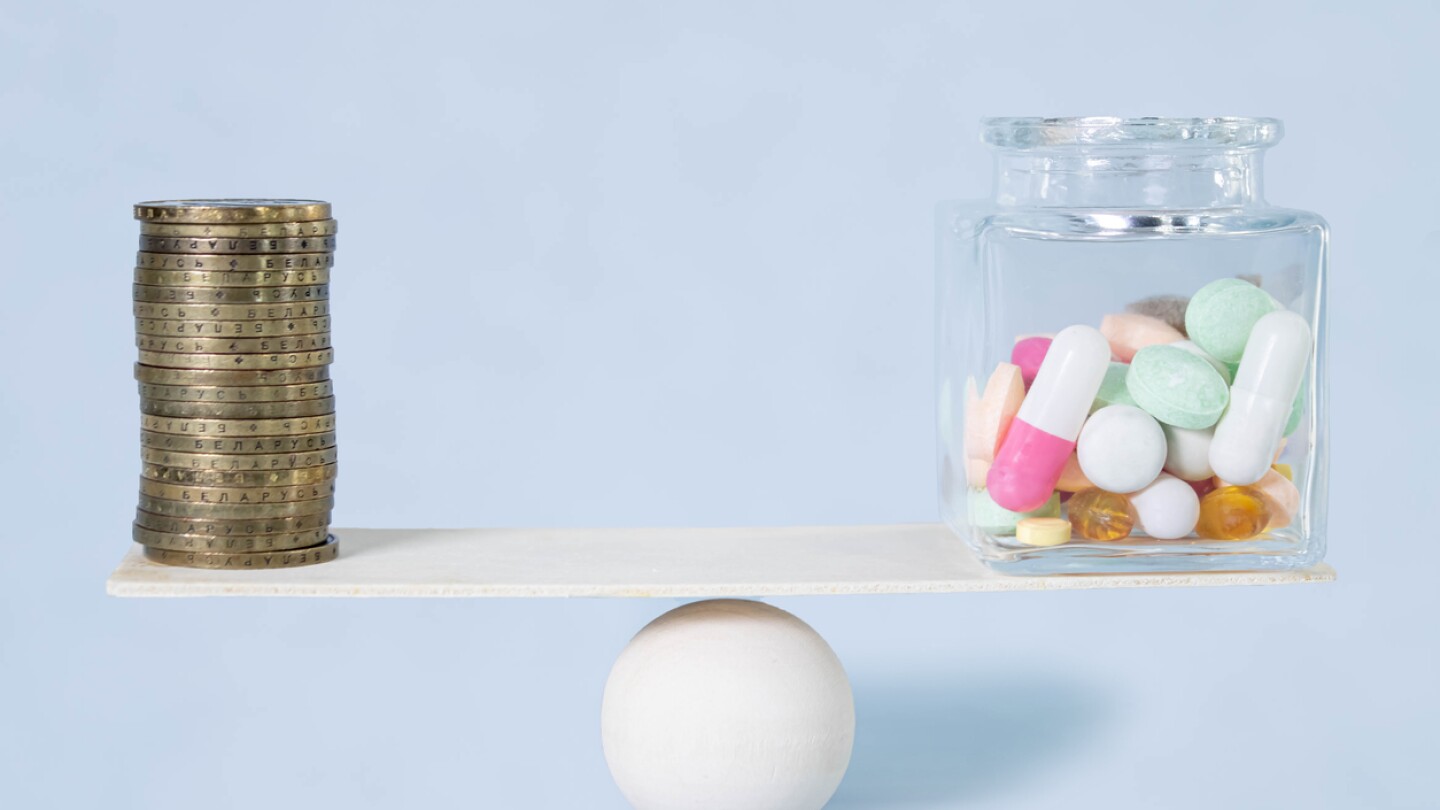Stack of coins balancing on seesaw over a bottle of pills.