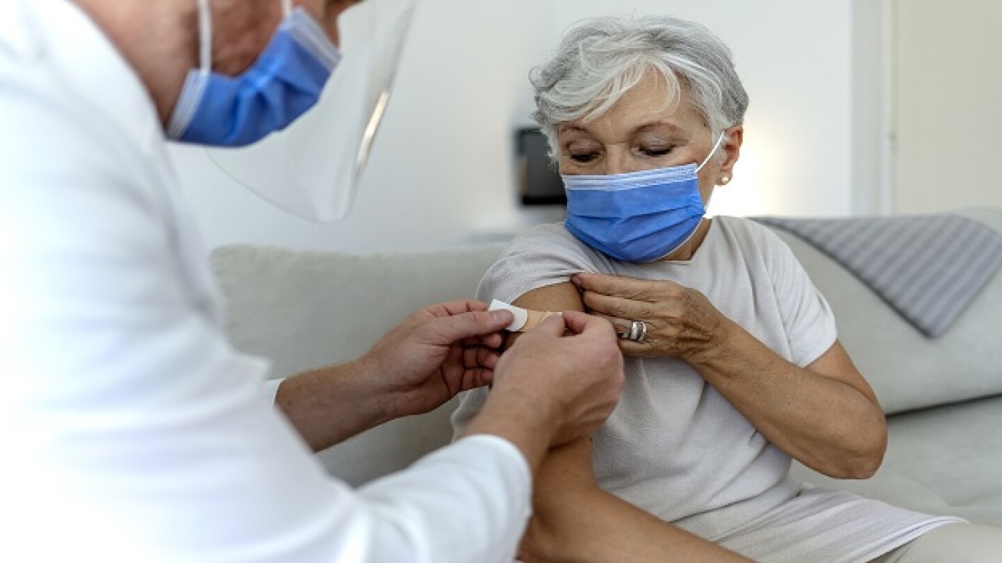 A male doctor puts a band aid on a senior woman's arm after he administered the COVID-19 vaccine injection. Close up image of elderly woman having vaccination. Coronavirus, medical exam, consultation.
