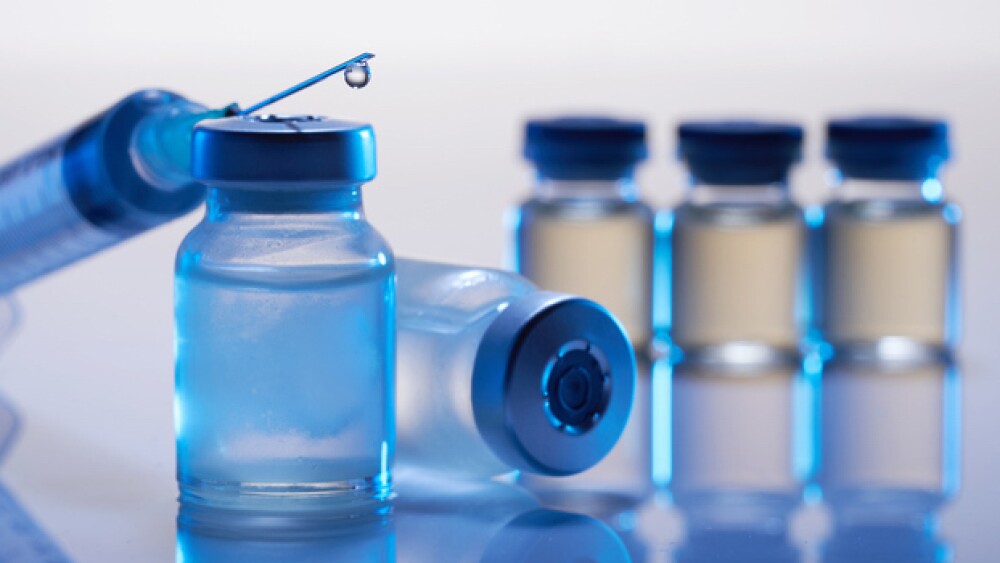 Syringe resting on top of a vaccine vial, with more vaccine bottles in the background