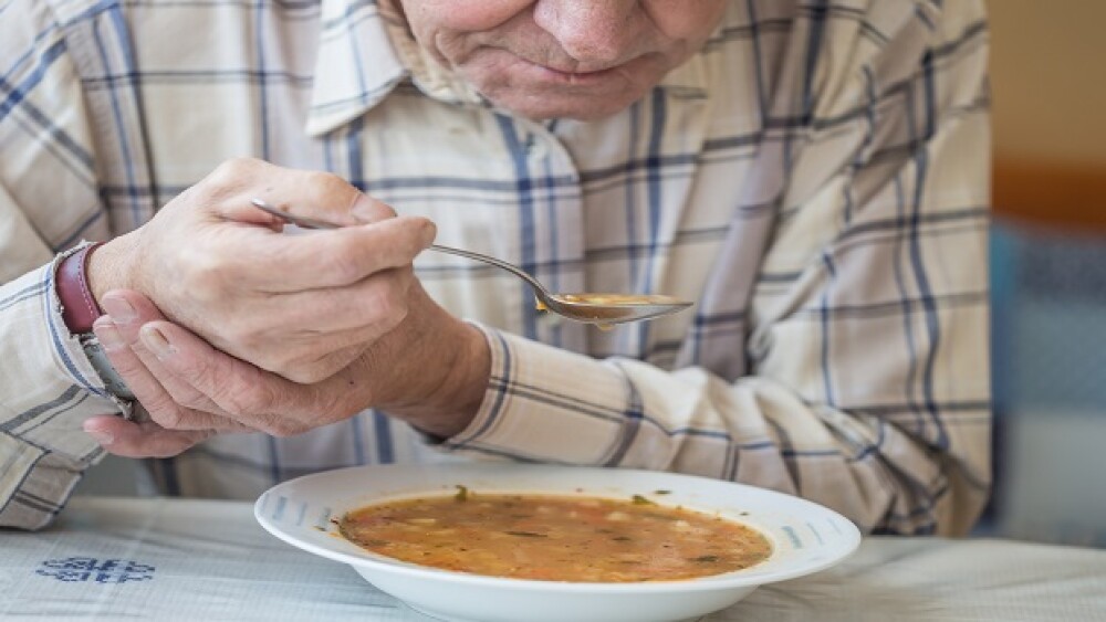 Elderly man with Parkinsons disease holds spoon in both hands.