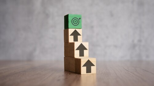 A stack of wooden blocks with arrows pointing upwards and target board. Mission, focus, ladder of success concept.