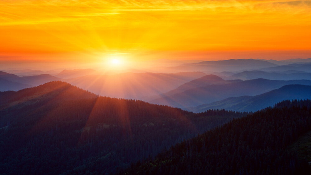 Amazing mountain landscape at sunrise, scenic view of silhouettes of the Carpathian mountains range, fantastic colorful sky with clouds and rising sun, outdoor travel background suitable for wallpaper