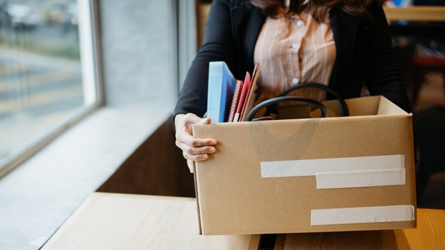 Asian woman holding cardboard box containing personal belongings after being fired by employer