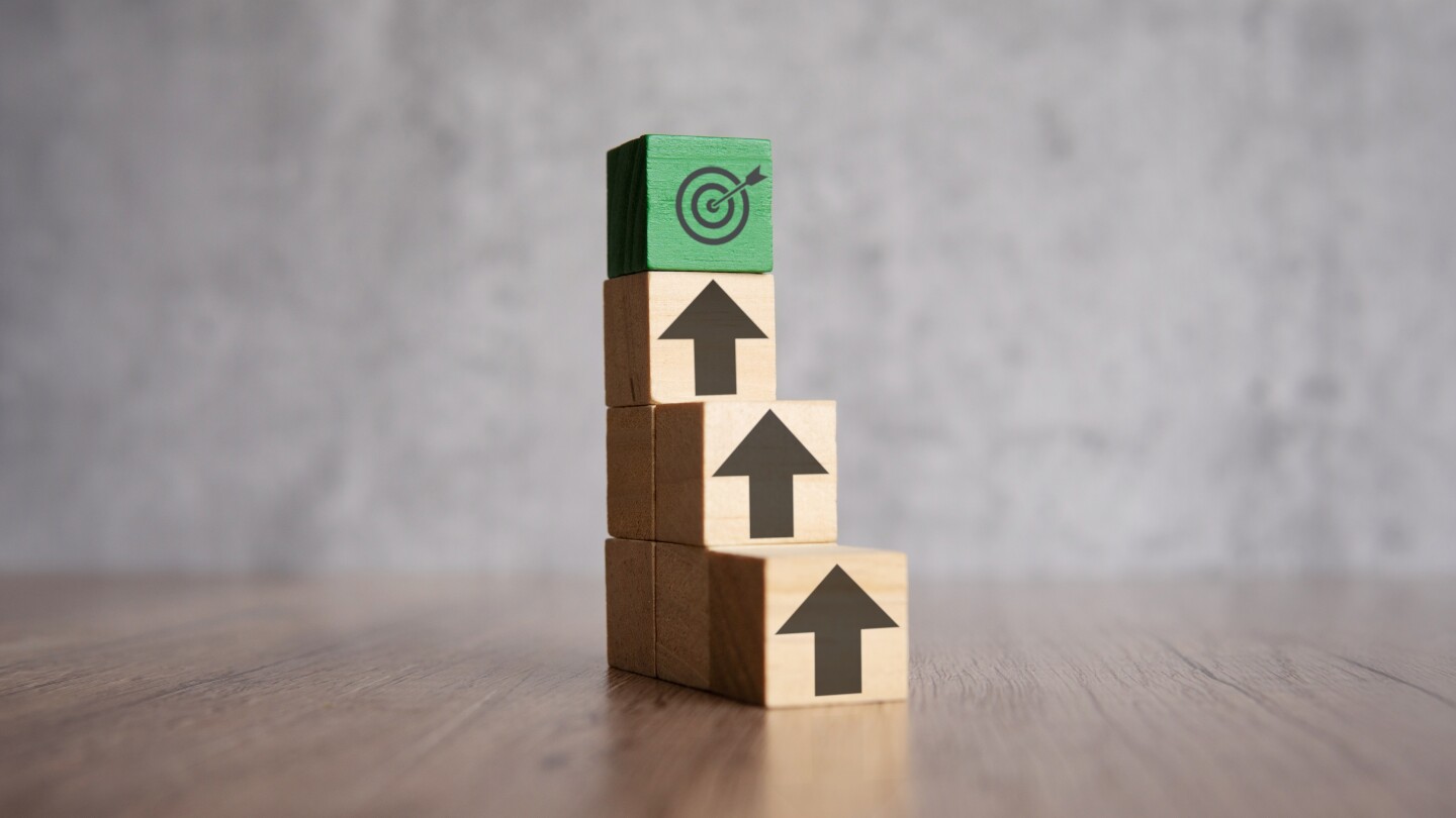 A stack of wooden blocks with arrows pointing upwards and target board. Mission, focus, ladder of success concept.