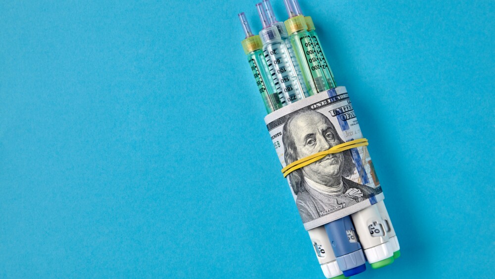 Insulin syringe pens wrapped in dollar bills on a blue background. Pharmaceutical monopolists raise drug prices. Top view with copy space