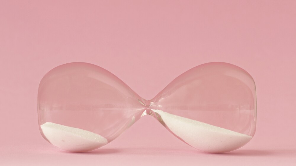 Hourglass lying on pink background - Concept of time and woman