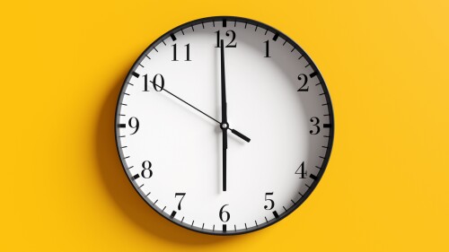 Round black and white wall clock at almost 6 o'clock on yellow background. Illustration of the concept of wake up time and off duty time