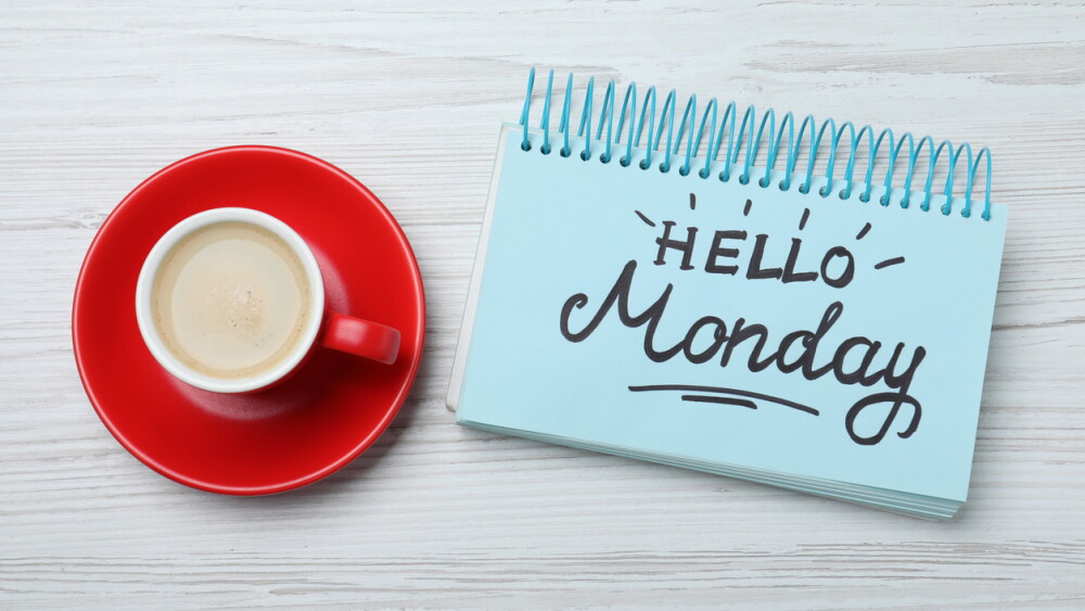 Message Hello Monday written in notebook and cup of coffee on white wooden desk, flat lay