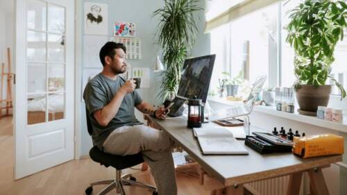 Photo shows man drinking coffee and working remote