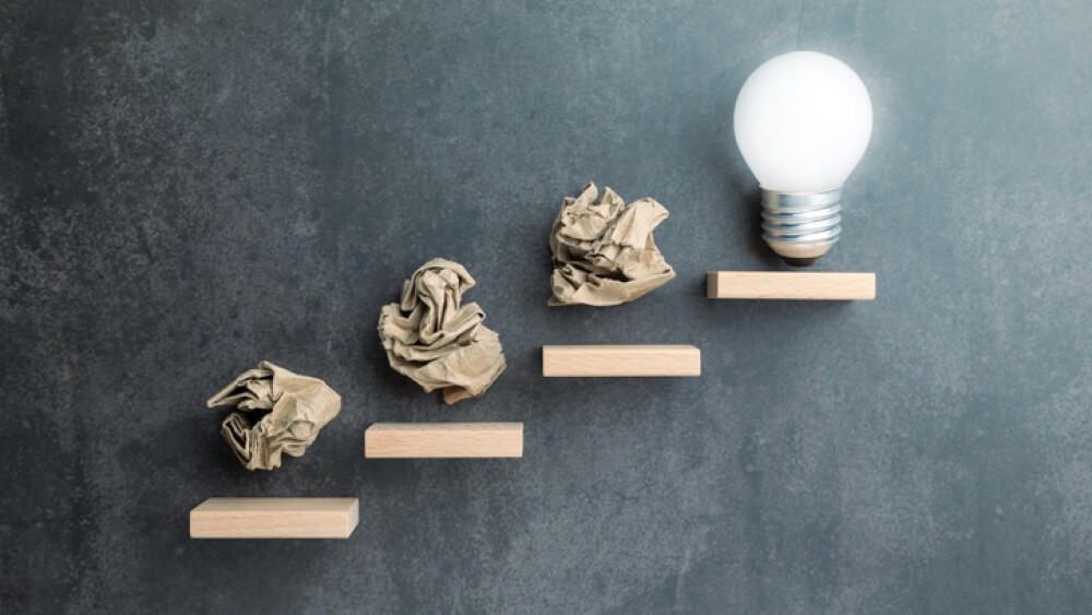 Conceptual image of crumpled paper balls as steps leading to a light bulb, symbolizing failure as part of the creative or problem-solving journey toward success