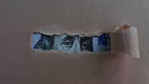 Paper torn and revealing dollar bill. Financial investment and cash income