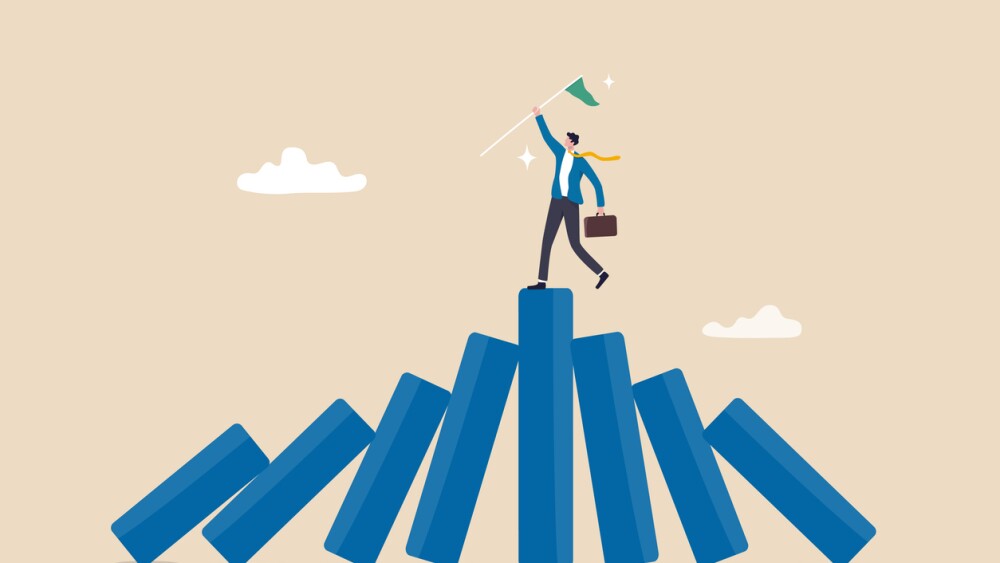 Illustration of businessman with flag looking victorious on top of teetering blocks