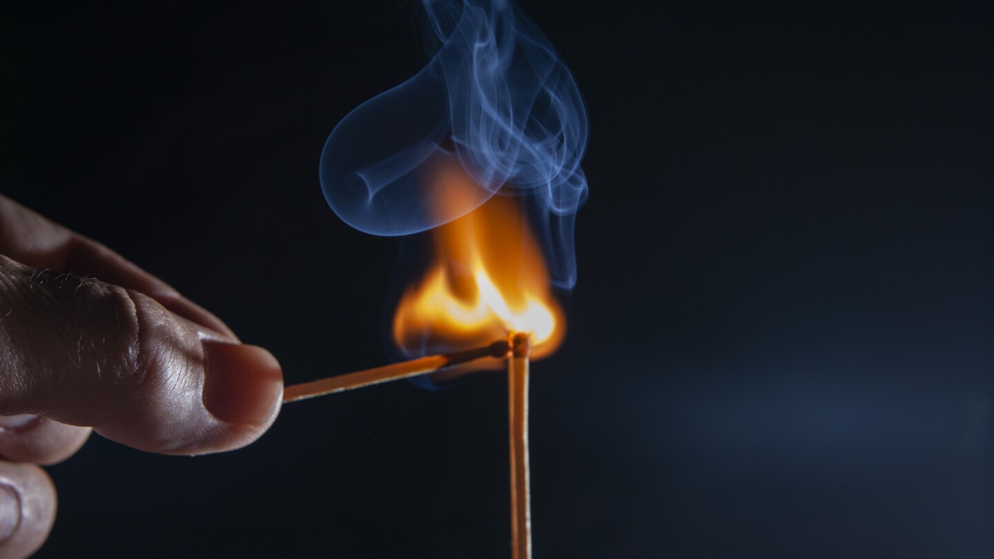 a hand with a lit match lighting another match