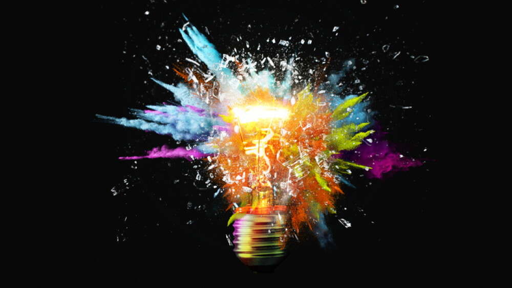 Creative light bulb explodes with colorful paint splashes and shards of glass on a black background. Think differently creative idea concept. Dry paint splatter. Brainstorm and think