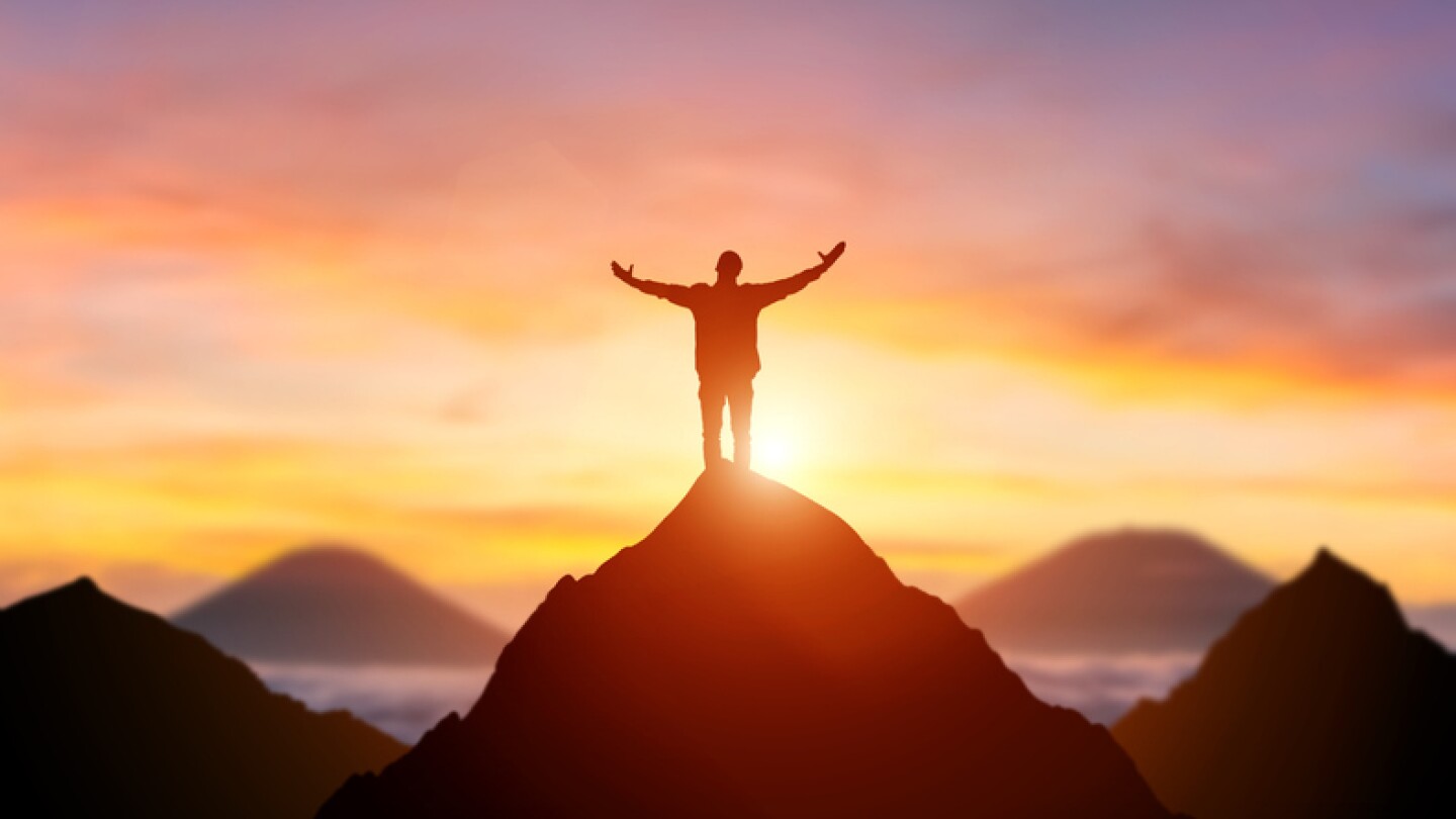 Silhouette of a business person on the top of a mountain peak in sunset background. Winner and conquer of businessman concept.