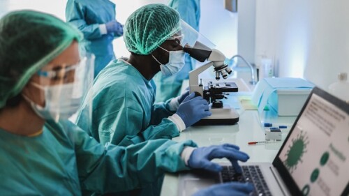 Multiracial medical scientists in hazmat suit working with microscope and laptop computer inside modern laboratory hospital - Focus african man face