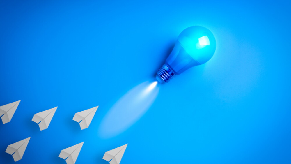 Creative concept of leadership and innovation with a glowing blue light bulb leading paper planes. Symbol of advanced technology, AI-driven strategy, and visionary direction in a digital future.