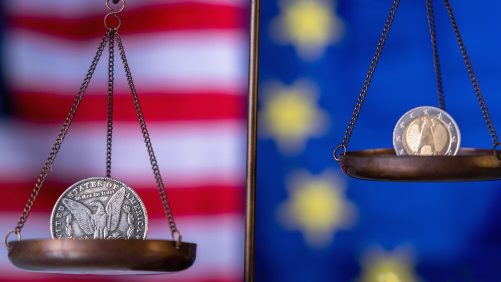 US Dollar coin and EU currencies on weighing scale against Unated States and European Union flags as symbol of trade war, economic conflict. Selective focus on Dollar.