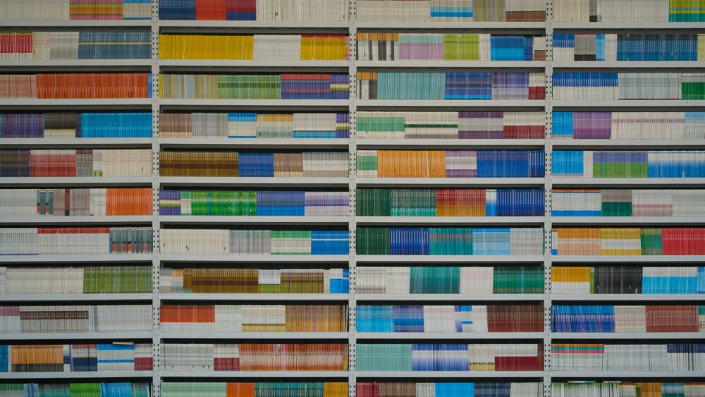 A vibrant geometric pattern of colorful book spines arranged neatly on shelves. This texture represents organized knowledge and information storage. The minimalist composition and bright colors are ideal for educational, corporate, or creative graphic design projects.