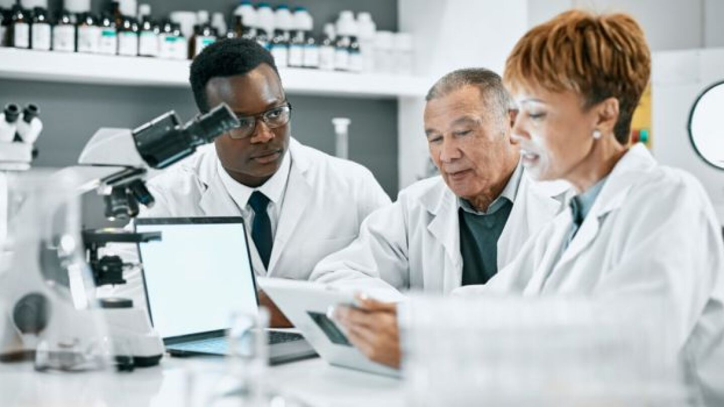 Pictured: Diverse group of biopharma employees collaborate in lab