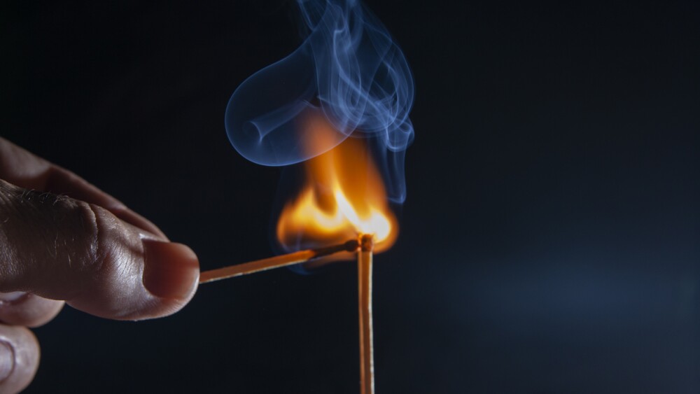 a hand with a lit match lighting another match