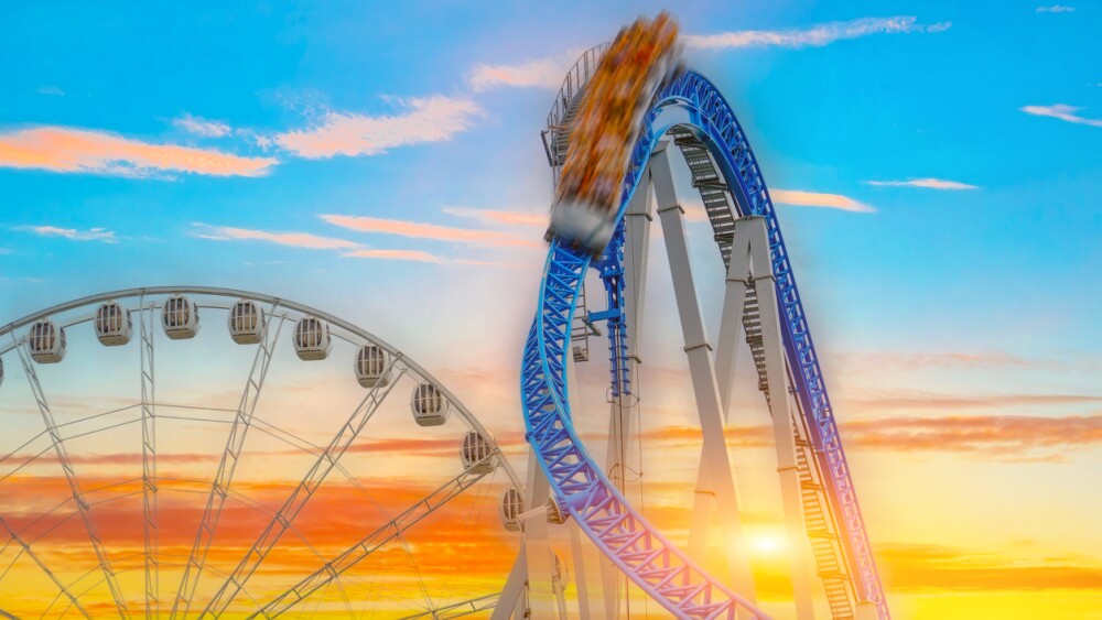 Roller coaster with carts falling speed motion blur down and screaming people against the background of Ferris wheel in amusement park sunset sky clouds