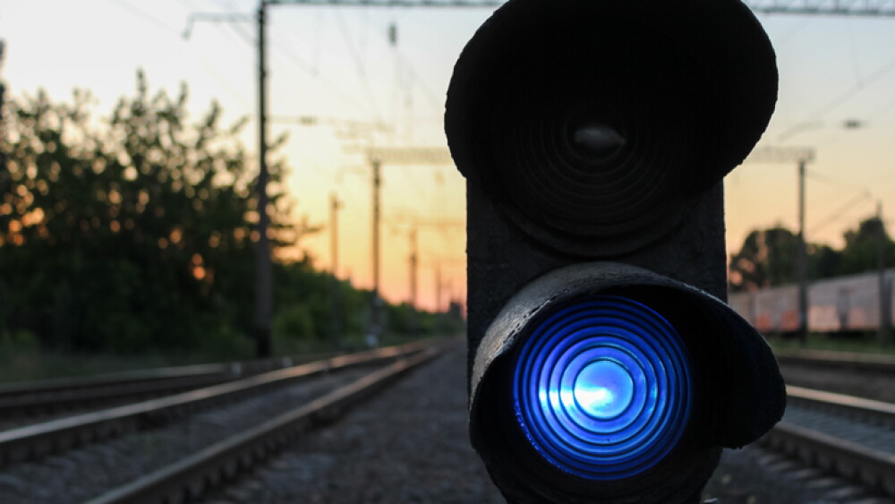 Close-up view of a vivid blue railway signal light illuminating a track at golden hour sunset, providing crucial safety guidance for efficient train operations and future transportation