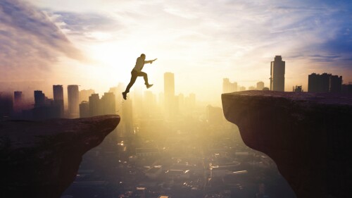 Young businessman jumping through gap cliff at sunrise time with modern city background