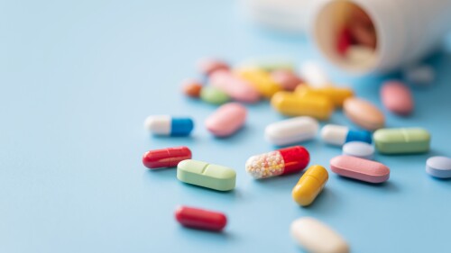 Colorful Pills scattered from white plastic pill bottle on blue background.