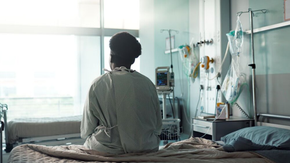 Image Credit: A female sits alone in a hospital waiting for medical treatment/ Jacob Wackerhausen for iStock