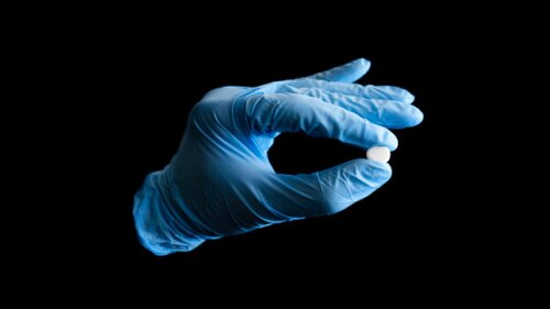 A white pill being held by a hand wearing a blue surgical glove. Medicine or drugs isolated on a black background.