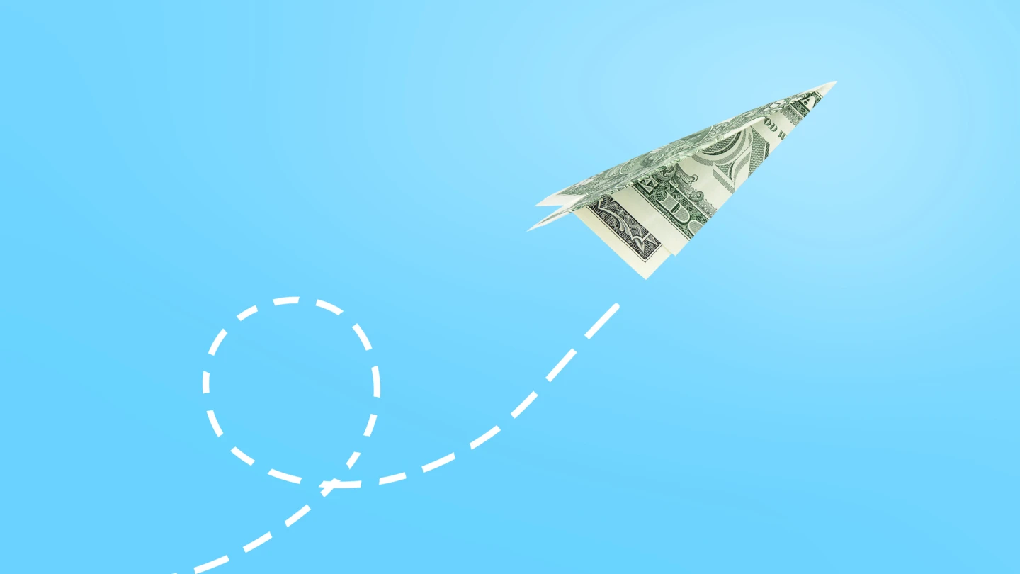 Dollar paper airplane flying against blue background, business concept