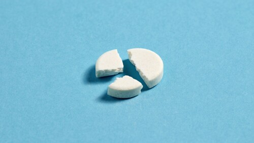 Reducing the dose of medicine. Splitting the pills. Health care and medication. White medical pill broken into three pieces on blue background.