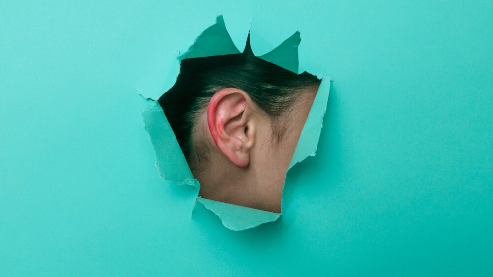 Female ear in paint close-up. Copy space. Torn paper, blue background. The concept of eavesdropping, espionage, gossip and the yellow press.