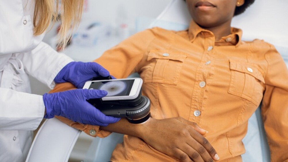 Preventive checkup, skin melanoma days concept. Close up of hands of female doctor dermatologist oncologist holding new generation dermatoscope, examining birthmarks and moles of afro lady