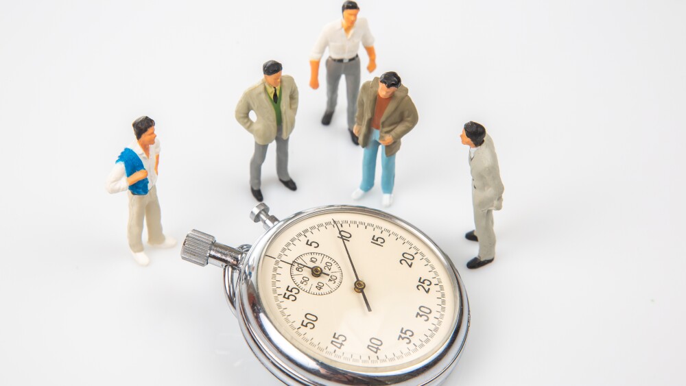 Four miniature figurines of men in casual and formal attire stand around a large stopwatch showing zero, symbolizing time management or competition.