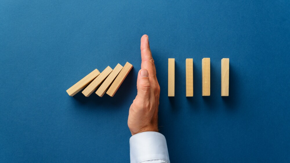 View from above of male hand interfering collapsing dominos in a conceptual image of business crisis management. Over navy blue background.