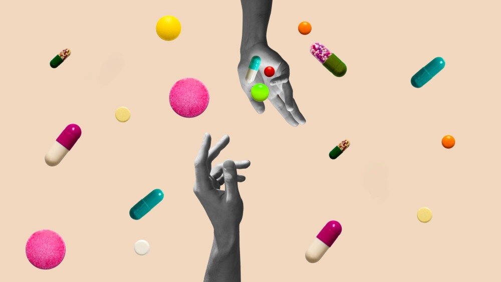 Hands in black and white dropping a collection of pills on a pink background