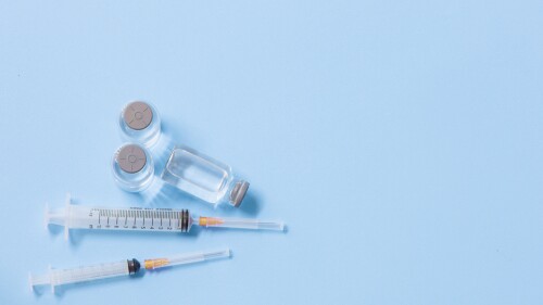 Close-Up Of Syringe With Bottles Against Blue Background