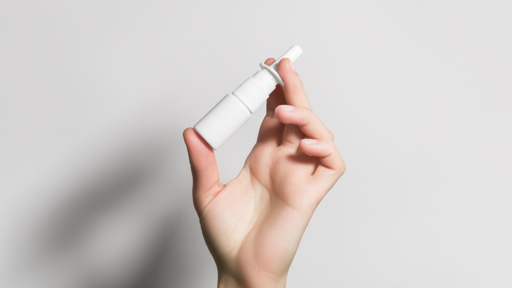 Hand holding a nasal spray bottle against a white background