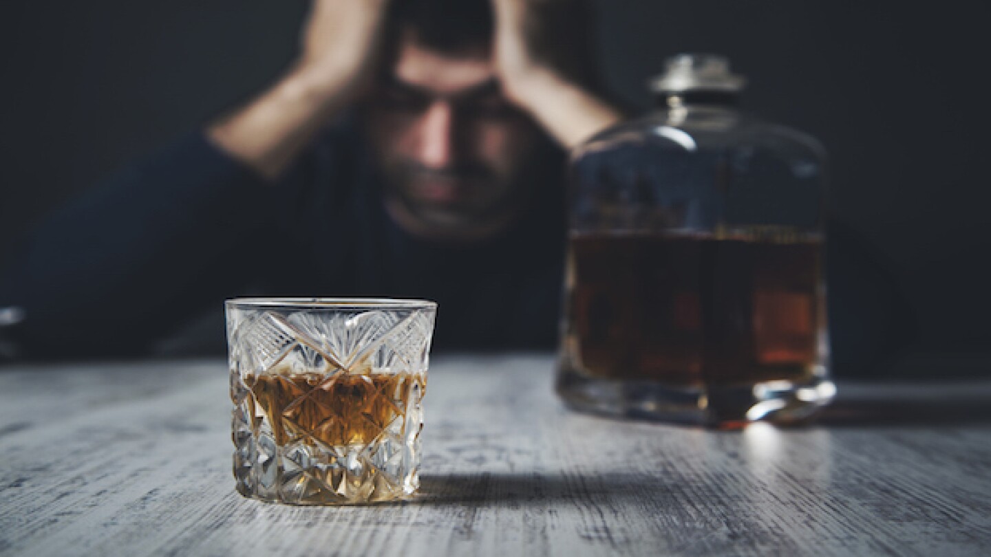 sad man hand in head with whiskey on desk