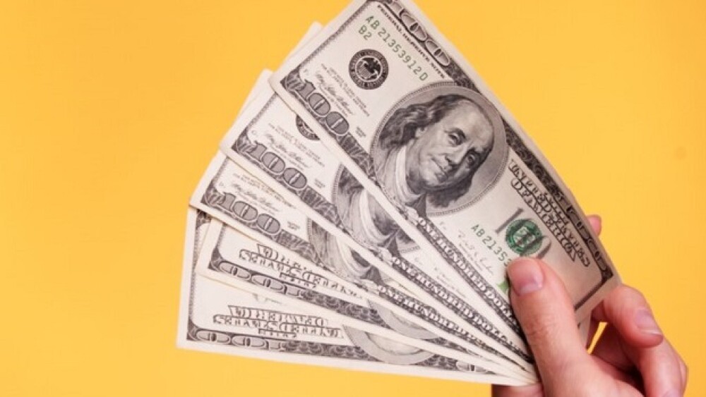 Woman holding 500 dollars against a yellow background.