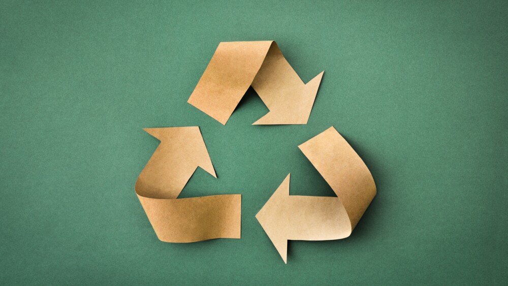 Recycling symbol with arrows made of brown paper on a green textured background. Top view.